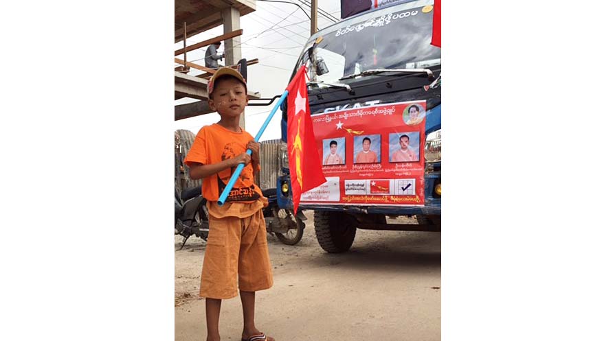 Photo of a boy waving an NLD flag in front of a parked van. 