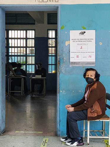 Woman sits in a chair against a blue wall at a polling station in Venezuela