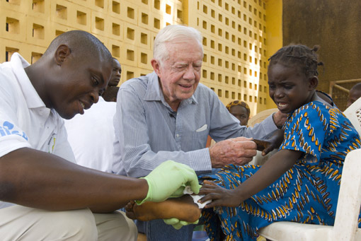 Former U.S. President Jimmy Carter comforts six-year-old Ruhama Issah as Adams Bawa, a Carter Center technical assistant, dresses her extremely painful Guinea worm wound.