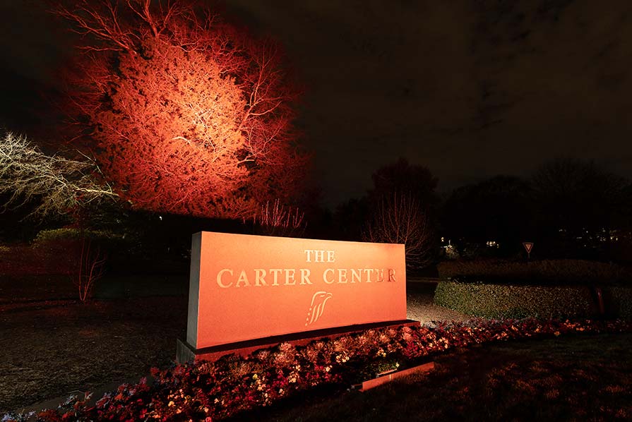 Photo of The Carter Center entrance sign illuminated with orange light.