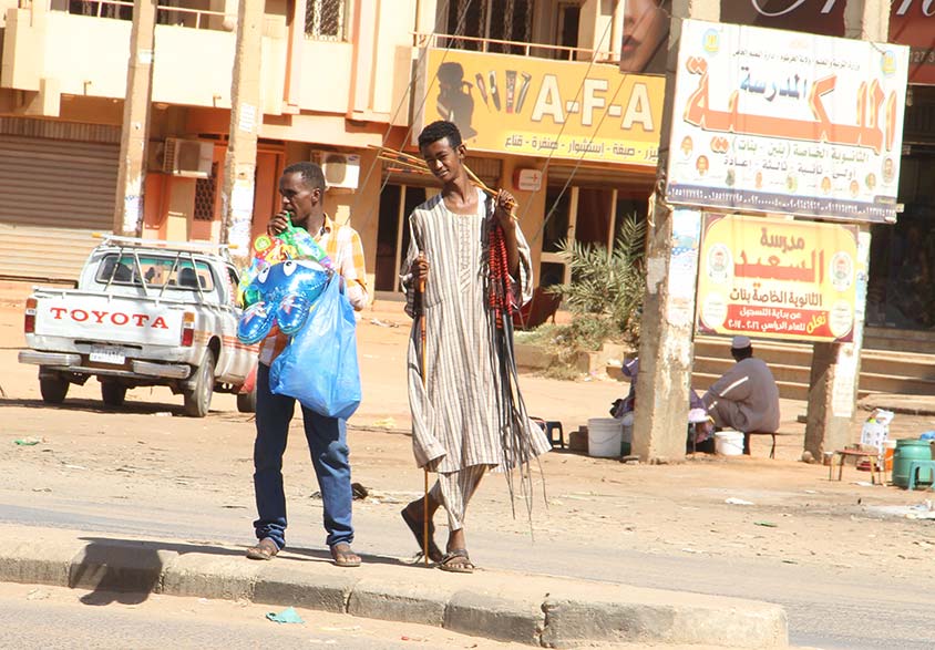 Photo of two young male Sudanese street vendors toting merchandise to be sold.