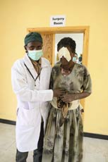 Dr. assists Ethiopian woman who has bandages over both eyes.