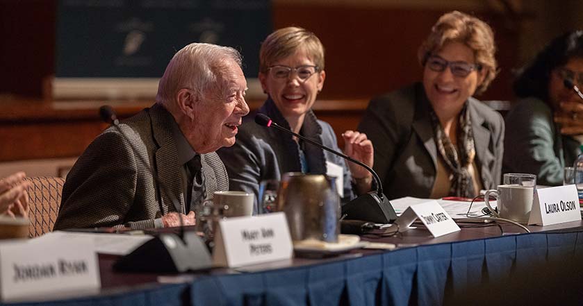 Jimmy Carter seated at a conference table speaking at a mic