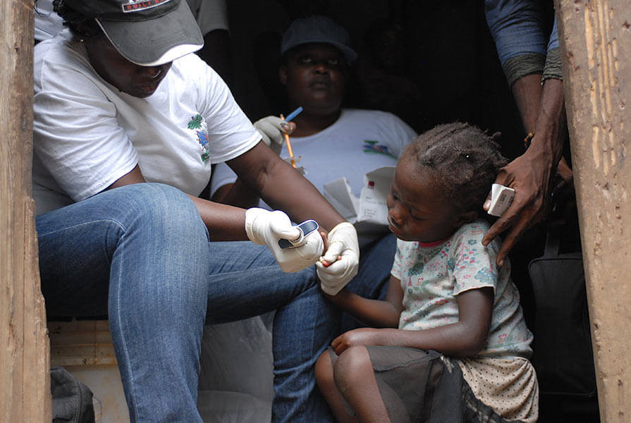 A squeamish Christmene, age 7, tries to sit still while a health worker draws a tiny drop of blood from her finger.