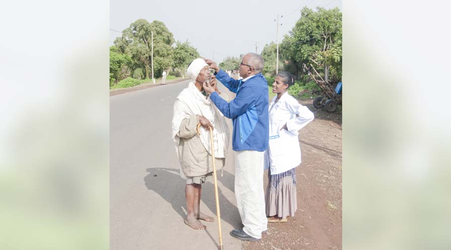 Mulat Zerihun examines a man's eyes as they stand off the side of a road. A woman looks on.