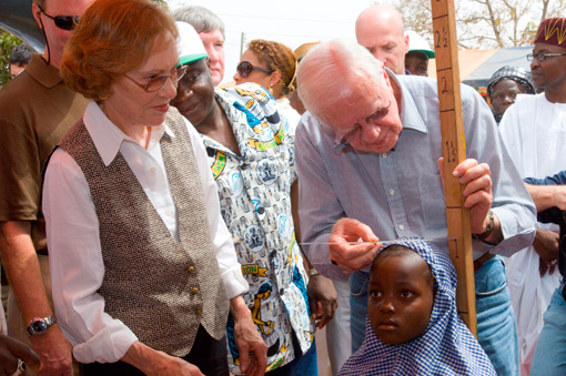 Former U.S. President Jimmy Carter and Carter Center CEO and President John Hardman measure a little girl's height to gauge the accurate medication needed to prevent schistosomiasis.
