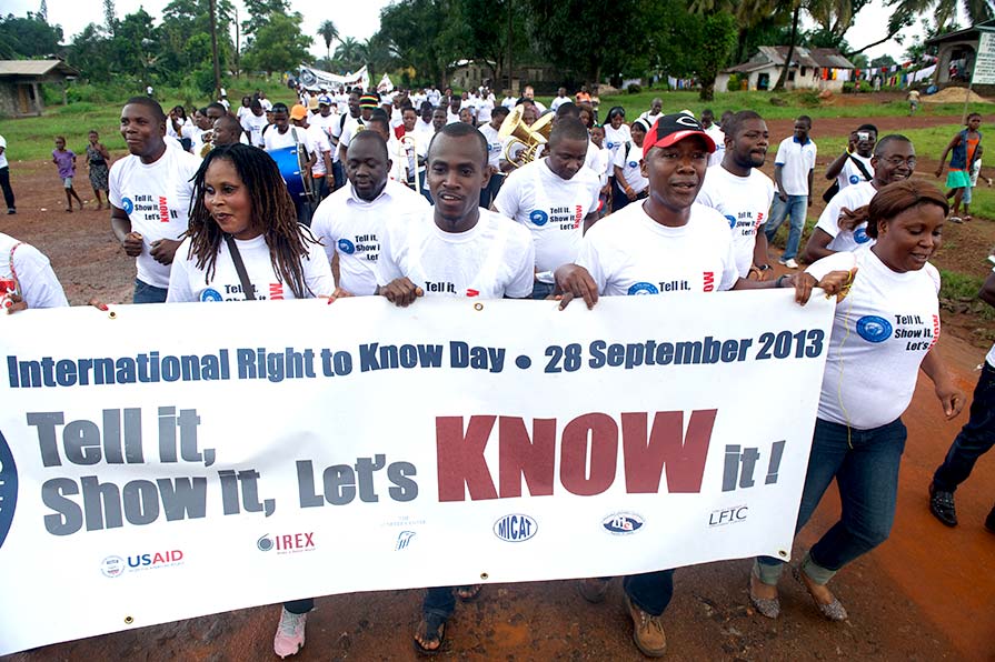 Photo of participants marching in a parade while holding an International Right to Know Day banner.