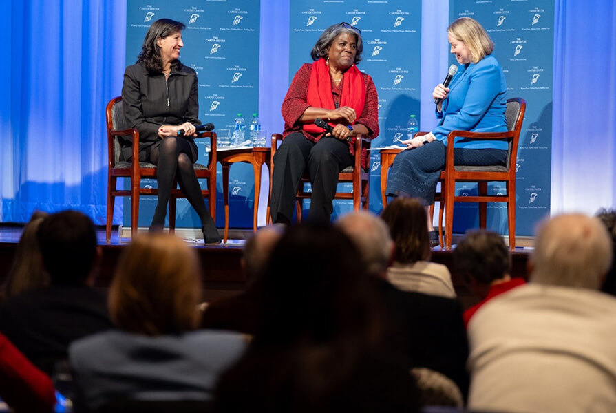 Three women sit on a stage at a conference.