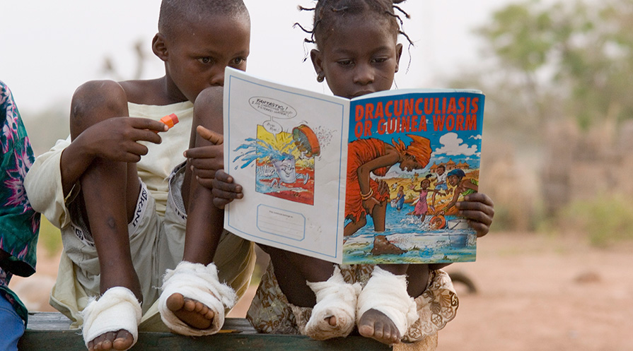 Two children with Guinea worm disease read a children’s book about the disease.