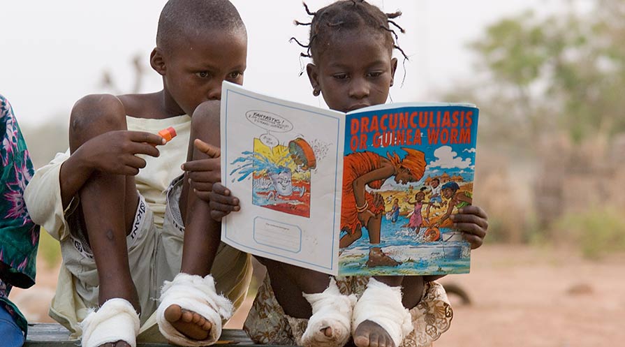  An educational comic book captures the attention of Guinea worm patients Sadia Mesuna (right) and Fatawu Yakubu at a case containment center in Ghana in 2007. (Photo: The Carter Center/L. Gubb)
