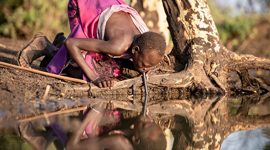 A villager from Achamungole Village, South Sudan, uses a filter to drink water at sunrise.