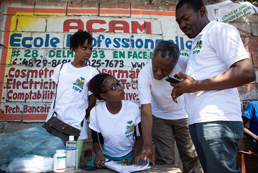 Dr. Madsen Beau De Rochars leans down to inspect records at a mass drug administration (MDA) post at a busy crossroads in Tabarre, Haiti. (Photo: The Carter Center/ H. Emanuel)