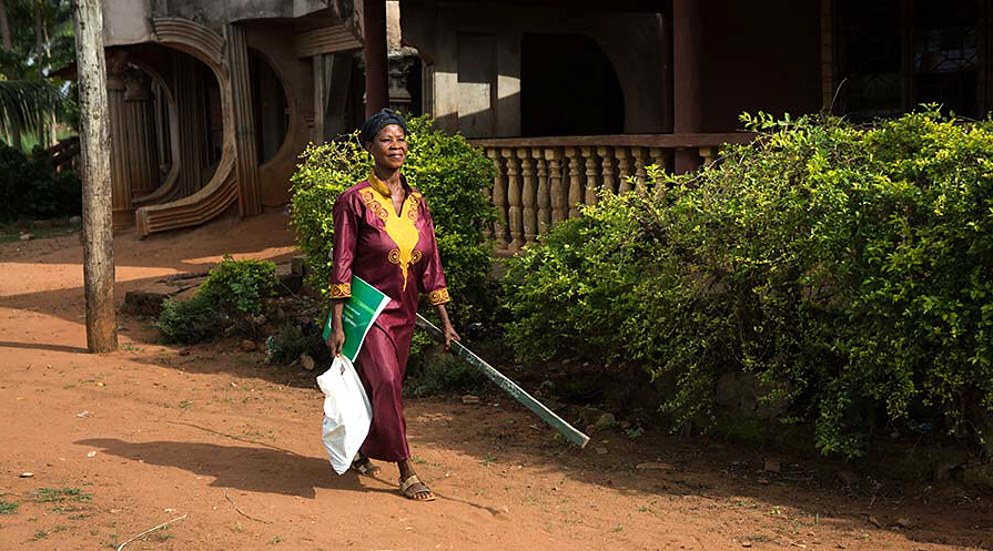 Photo of a woman walking down a dirt road in Nigeria carrying drug distribution supplies.