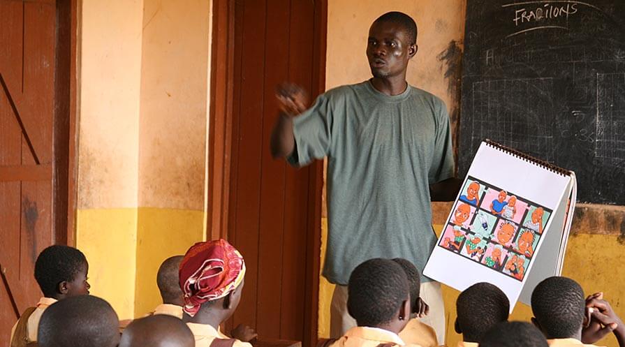 A health worker in Ghana leads a discussion about trachoma in a primary school. He uses the flip chart "Let's Be Trachoma Free" to encourage student participation.