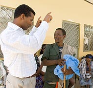 Dr. Estifanos Biru, the Carter Center's deputy country director (left), helps local health center staff educate Wolde how to hang his bed nets correctly to protect his family from malaria. 