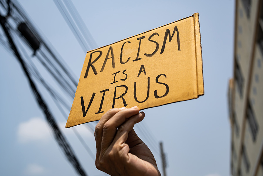 A hand holds a sign that says racism is a virus