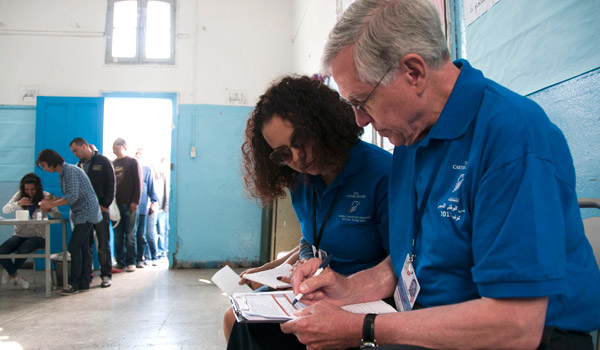 Delegation co-leader Dr. Hardman completes his observer checklist with translator Nedia Samet, as a voter inks her finger in the background.